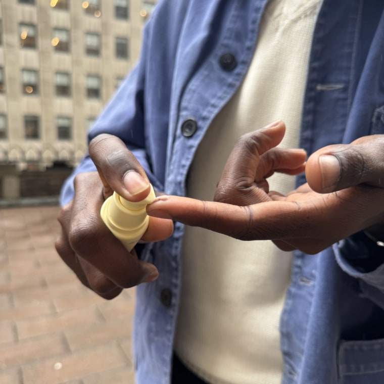 Bowman squeezing the Dr. Loretta sunscreen onto the tip of his finger with a building in the background.