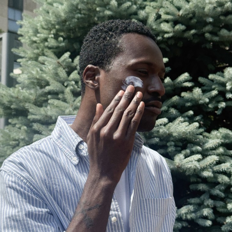 NBC Select editor in front of a green background, rubbing sunscreen formulas into their faces.
