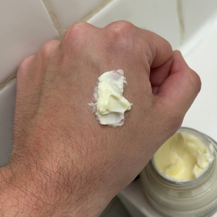 Person holding Bobbi Brown moisturizer and primer container with product on back of hand