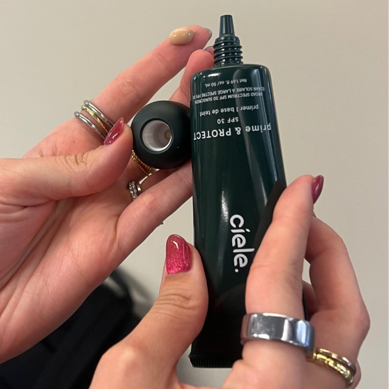 Woman holding Ciele primer packaging with dot of primer on finger