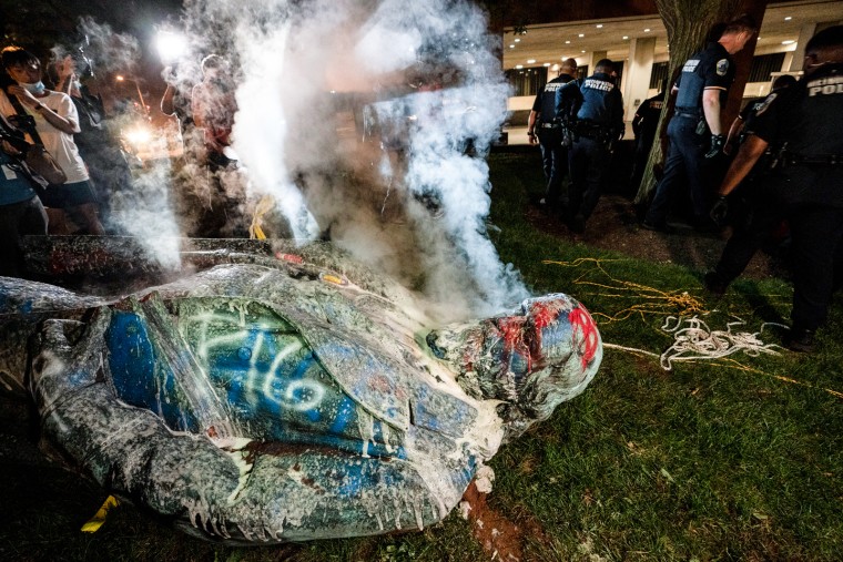 Police extinguish the burning statue of Confederate General Albert Pike toppled over on the grass
