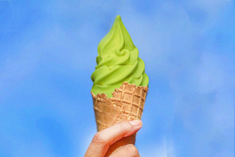 Ice cream cone with matcha soft serve against a blue sky 