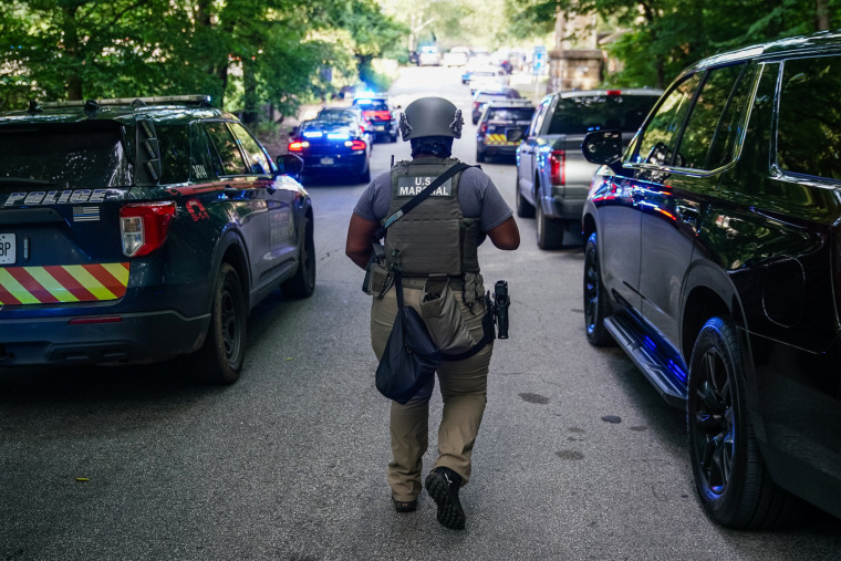 A U.S. Marshal walks down a street lined with police vehicles