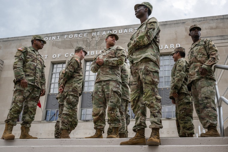 Members of the National Guard stand outside on steps in front of a building