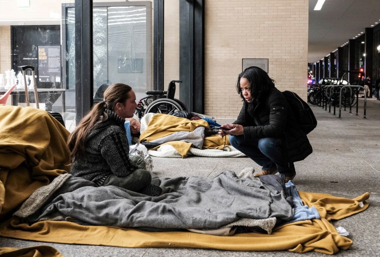 Rachel Pierre, right, speaks with a homeless woman sitting on a blanket outside