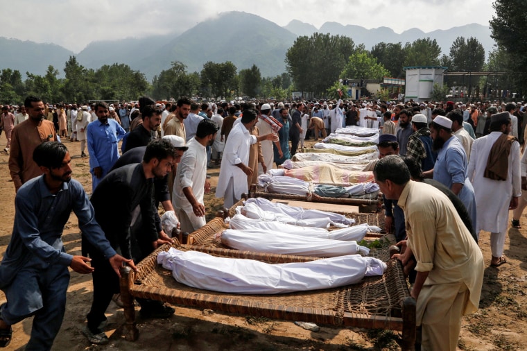 People arrange cots with the bodies of victims as they prepare for their funeral following heavy rain and floods in Buner district 