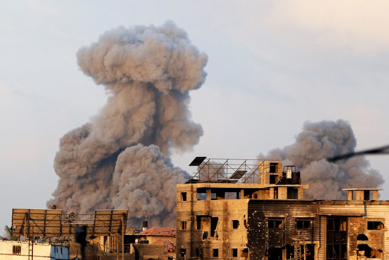 Palestinians stand as smoke rises following an Israeli strike, in Gaza City