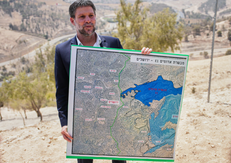 Bezalel Smotrich stand outside and holds a map that shows the E1 settlement
