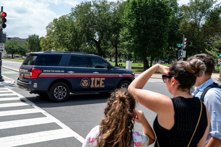 An Immigration and Customs Enforcement police SUV patrols on the road as people watch from the sidewalk