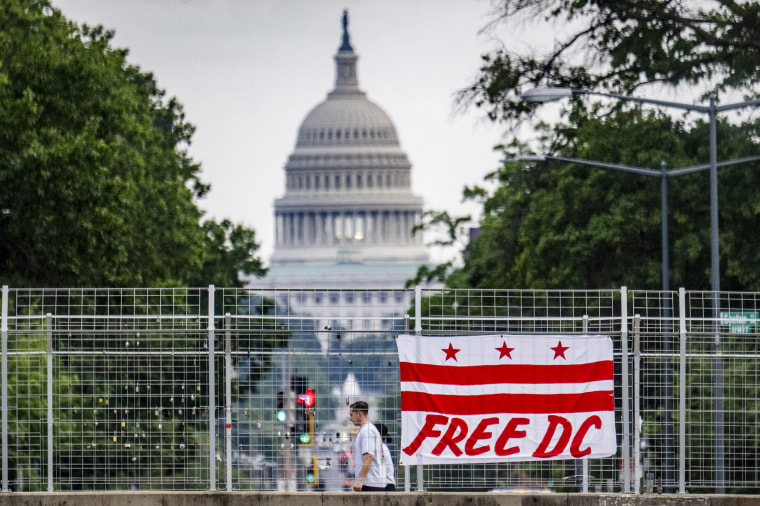 Image: Pedestrians walk past a flag that reads "Free DC" hanging on an overpass near the U.S. Capitol building