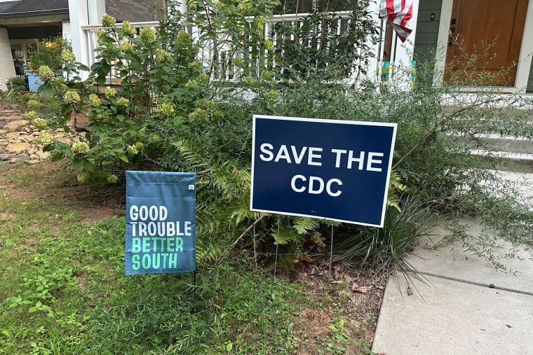 Two signs on a front lawn, one on the left says "Good Trouble Better South," and the one on the right says, "Save the CDC."