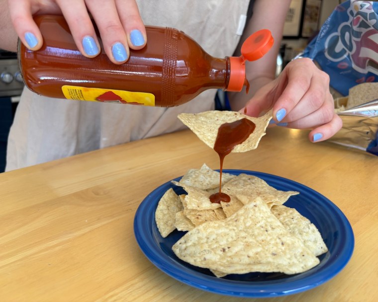A hand holding a bottle of Valentina Hot Sauce in front of a wood table.