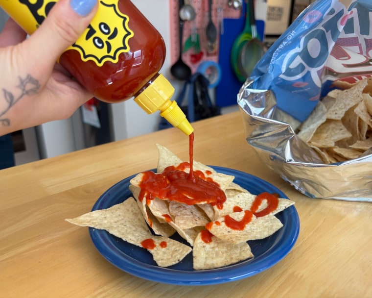 A hand squeezing a bottle of Yellowbird Classic Jalapeño Hot Sauce, adding some to a tortilla chip.