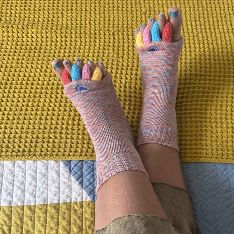 An overhead shot of a woman wearing Original Foot Alignment Socks on top of a colorful comforter