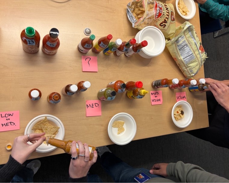 Hot sauces on a wood table with bags of tortilla chips.