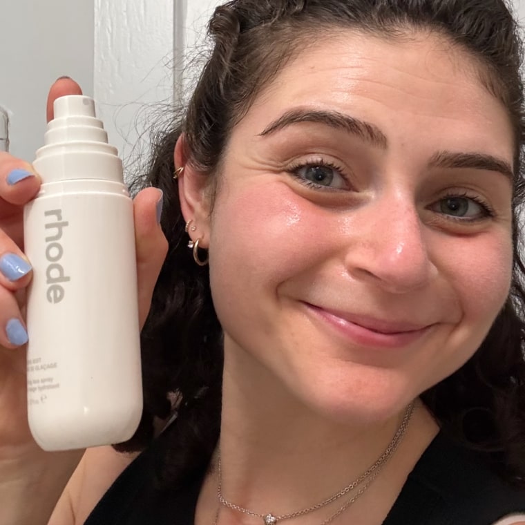 A photo of a woman smiling while holding a facial mist bottle in her hand