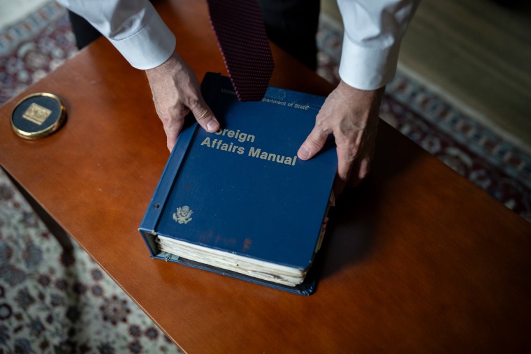 A large blue book titled "Foreign Affairs Manual" is on a wooden tabletop