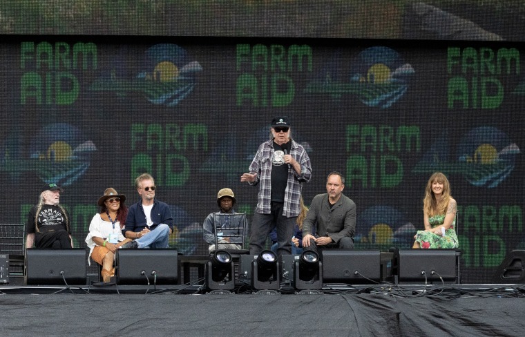 People sit on stage behind Willie Nelson as he speaks