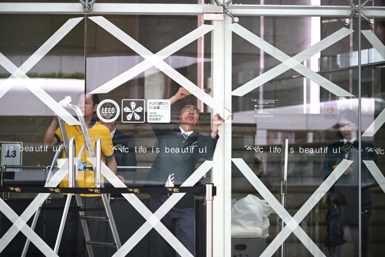 Workers tape up windows, using X shaped tape patterns across the glass
