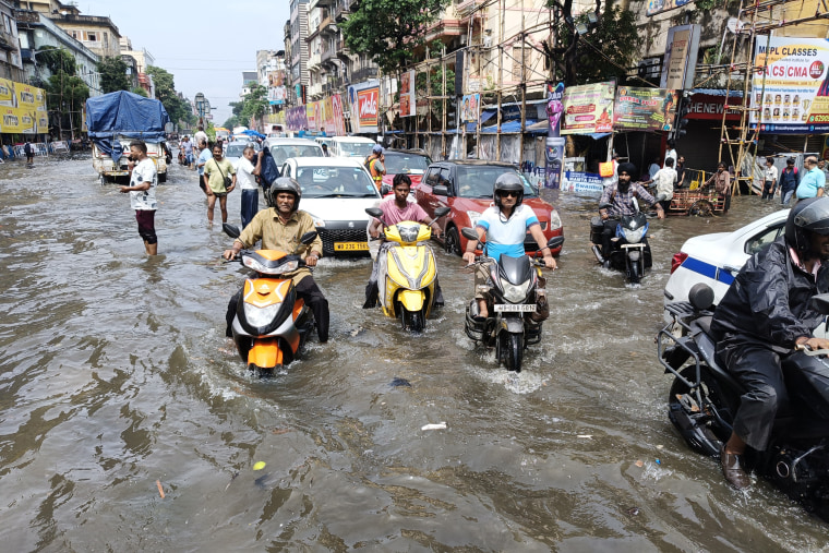 Three men drive motorbikes through a flooded road