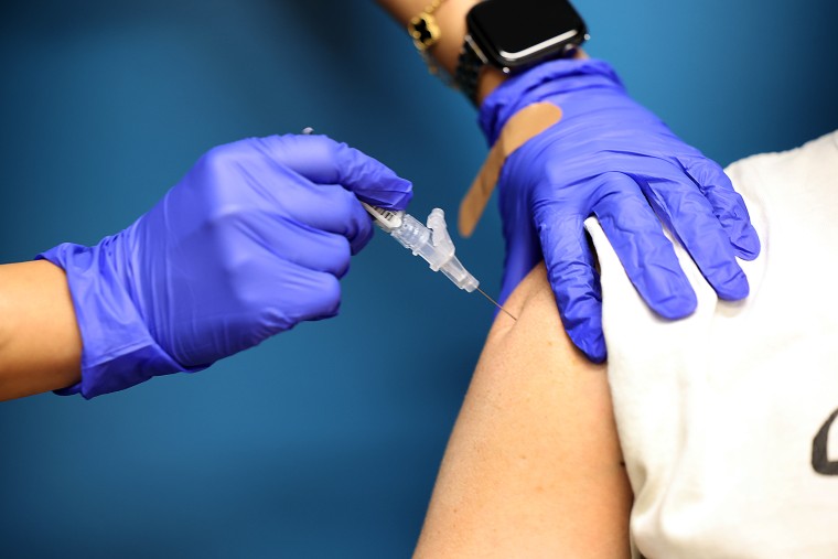 Gloved hands administer a vaccine to a persons shoulder.