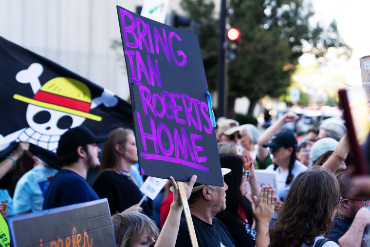 A protester holds a sign that reads "Bring Iowa Roberts Home"