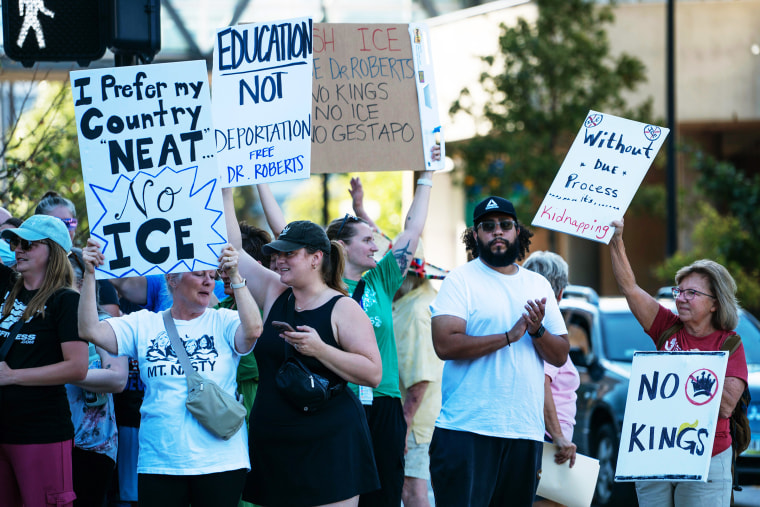 Community members hold posters that read, "I prefer my country neat, no ICE" and "Education not Deportation Free Dr. Roberts."