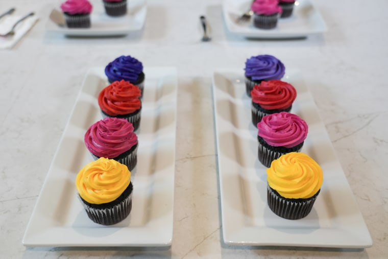 Two rows of multi-colored cupcakes on plates on a counter
