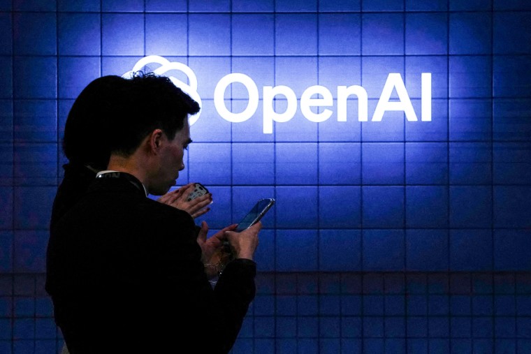 Visitors look at their phone next to an Open AI logo on a blue tiled wall