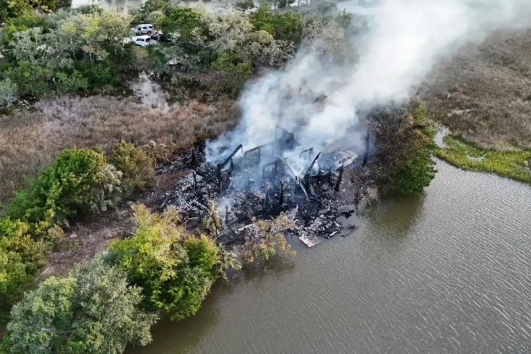 A aerial view of a home on fire, smoke billowing