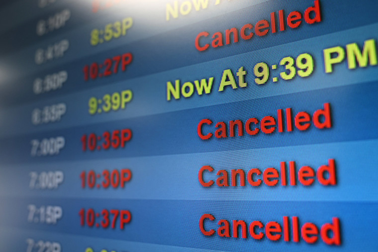 An arrivals board shows delayed and cancelled flights
