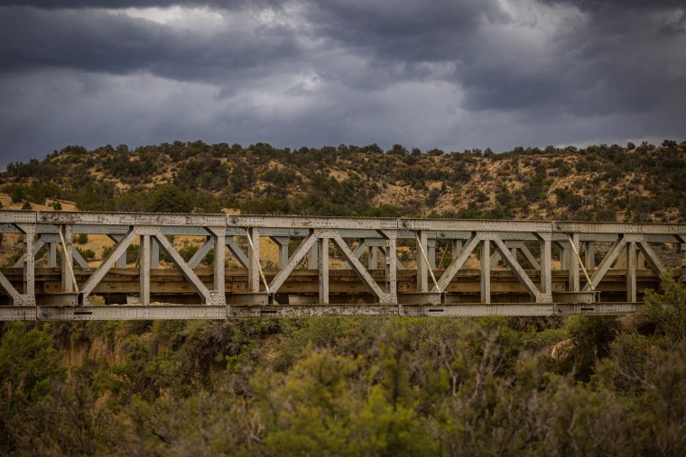A military surplus bridge seen from the side, outside surrounded by trees and mesas
