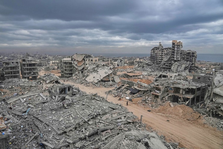 Displaced Palestinians walk amid destroyed buildings in the Shati refugee camp in Gaza City, Sunday, Oct. 12, 2025.