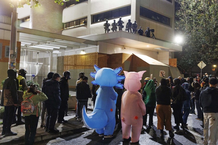 Protesters, including two in inflatable animal costumes, stand outside the ICE facility in Portland, Ore., on Saturday, Oct. 11, 2025. 