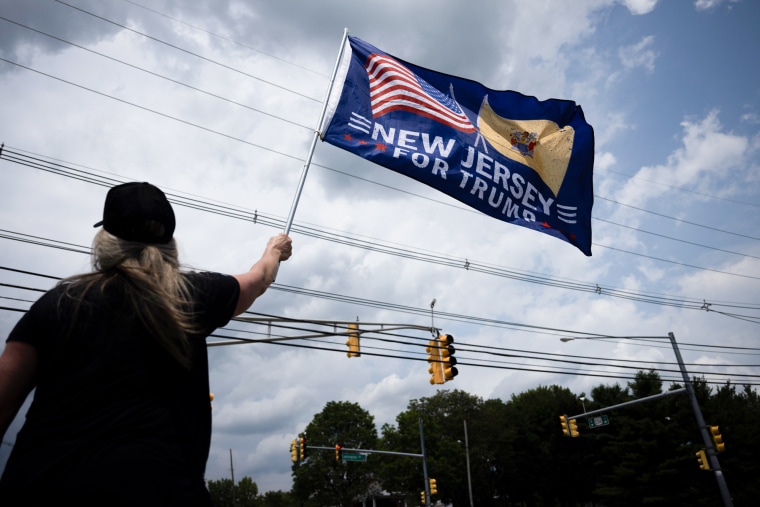 A person holds a flag outside that reads "New Jersey for Trump"