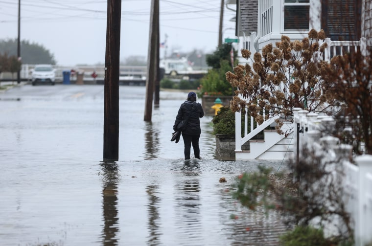 A person walks through flood waters on a sidewalk next to a house outside