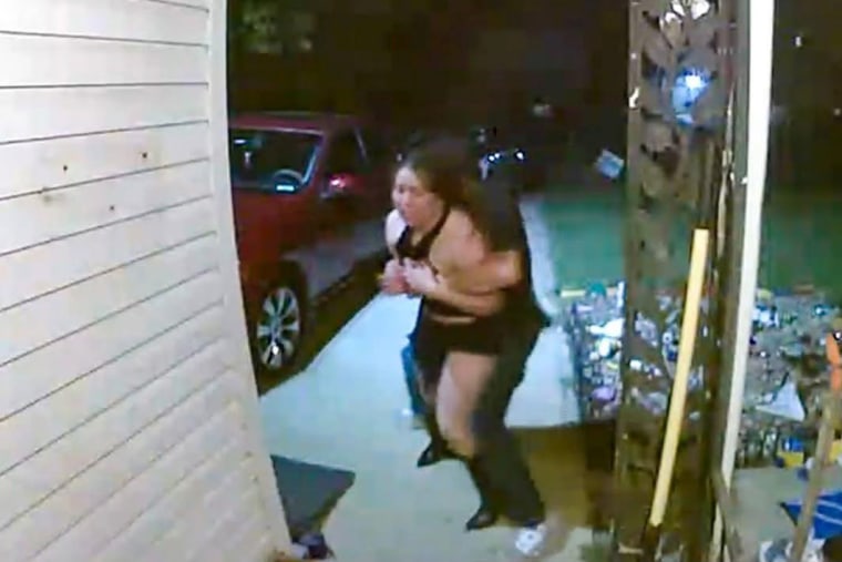 A video footage still of a woman being grabbed and taken by a man in front of a porch outside, in a driveway
