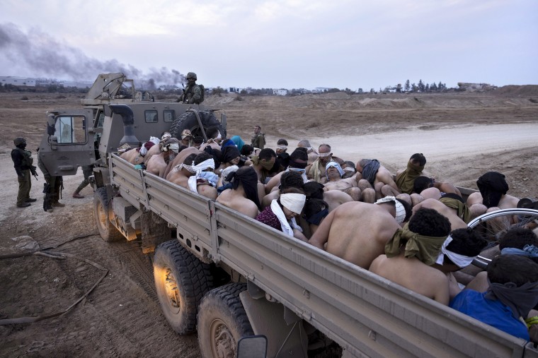 Israeli soldiers stand next to a truck full of bound and blindfolded Palestinian detainees in Gaza in December 2023.