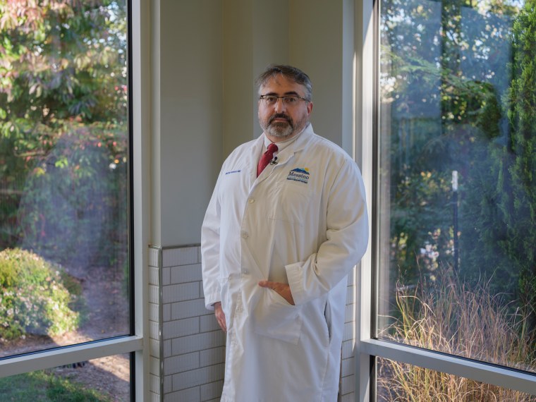 Martin Palmeri stands in the corner of a room between two large windows