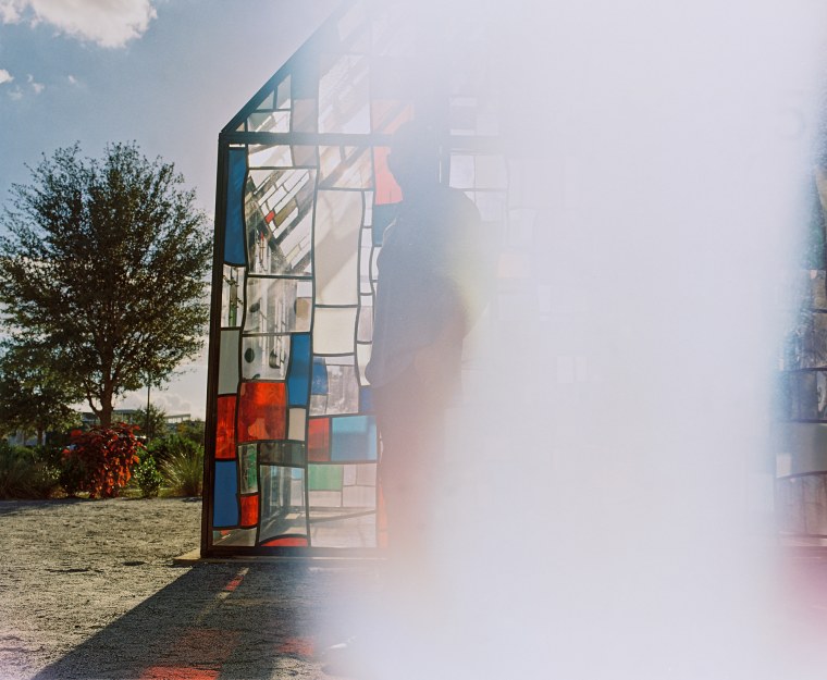 Giuseppe Corletto stands in front of a stained glass house, half of the image is covered by a white blur caused by film exposure