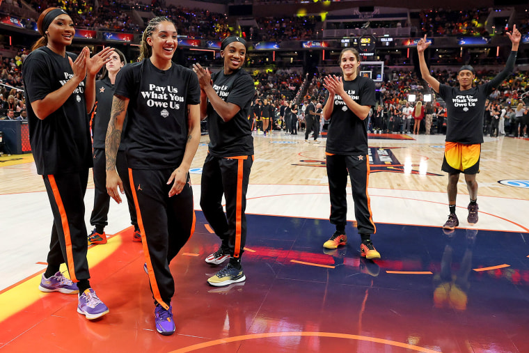 From left, Kiki Iriafen of the Washington Mystics, Gabby Williams of the Seattle Storm, Jackie Young of the Las Vegas Aces, Sonia Citron of the Washington Mystics and Brittney Sykes of the Washington Mystics wear shirts saying "Pay us what you owe us" prior to WNBA All-Star Game on July 19, 2025 in Indianapolis.