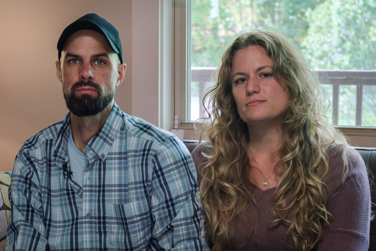 John Middleton and Caitlin Middleton sit next to each other on a couch, behind them is a window showing a view of the outside