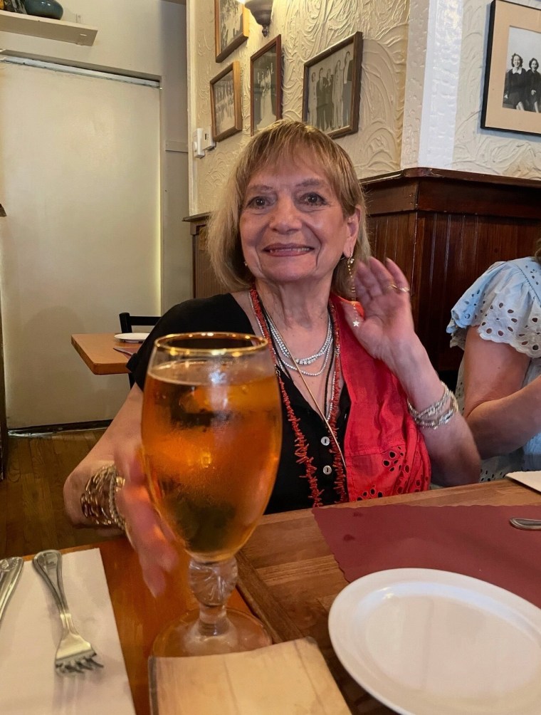 woman with red scarf seated at table with a glass of beer in front of her.