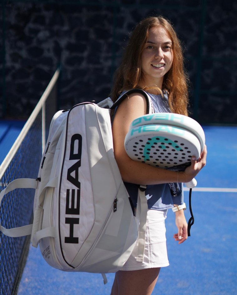Padel’s Popularity Is on the Rise. What To Know About the Sport’s Mexican Origins 2 Woman with red hair holds an athletic bag and two padel racquets.