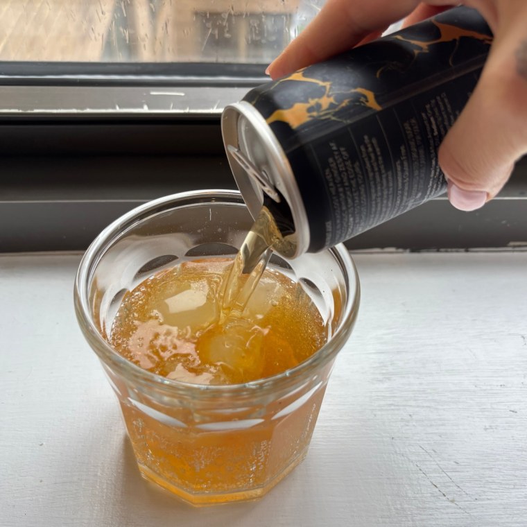 A hand pouring a can of Free AF’s Whiskey Ginger into a glass cup.