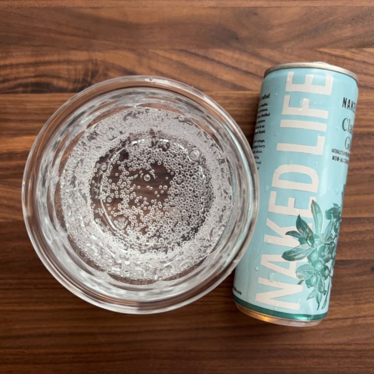 A can of Naked Life’s G&T lying down next to a glass cup filled with the drink.