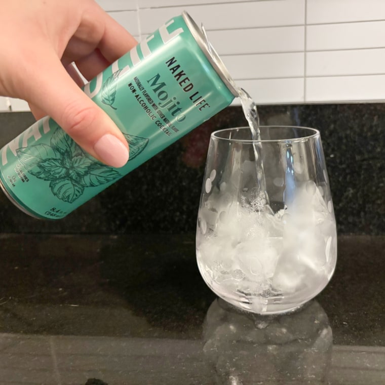 A hand pouring Naked Life’s Mojito into a glass cup.