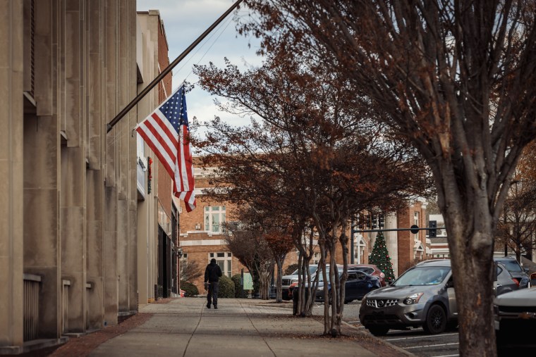 A view of the exterior of a building with an American flag on the side, facing a sidewalk and parking lot