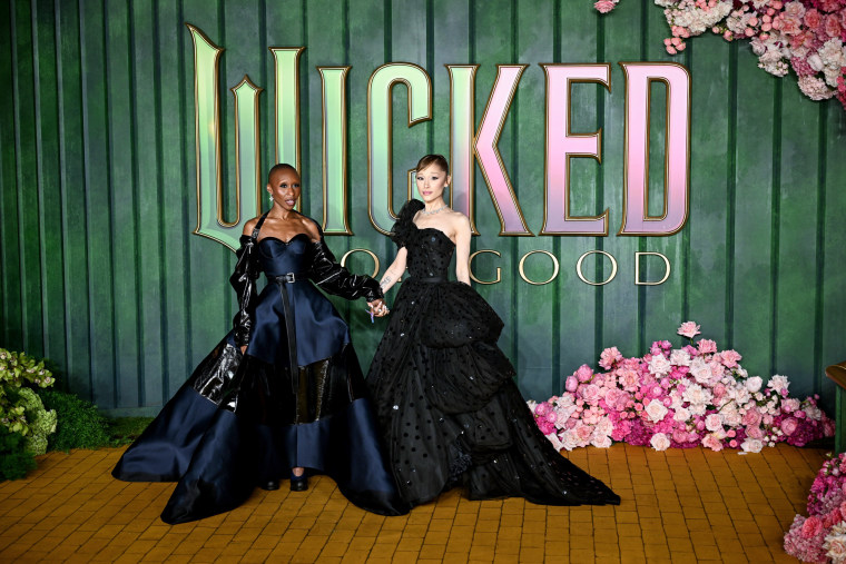 Cynthia Erivo, left, and Ariana Grande pose together in front of a green wall with text that reads "Wicked For Good"