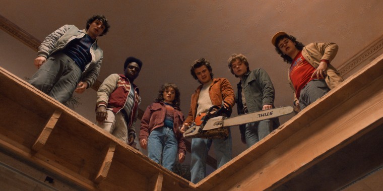 From left, Finn Wolfhard, Caleb McLaughlin, Natalia Dyer, Joe Keery, Charlie Heaton, and Gaten Matarazzo are seen standing on top of a wooden surface